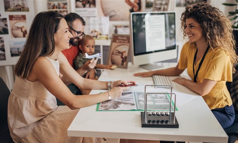 A woman and her family sit at a table reviewing documents with a Travel Professional at a modern office.