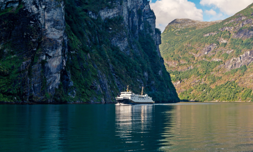 Un ferry glisse sur un fjord paisible, entouré de falaises imposantes et d'une végétation luxuriante.