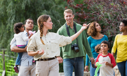 Group of people, including children and a guide, outdoors in a natural setting with trees and greenery.